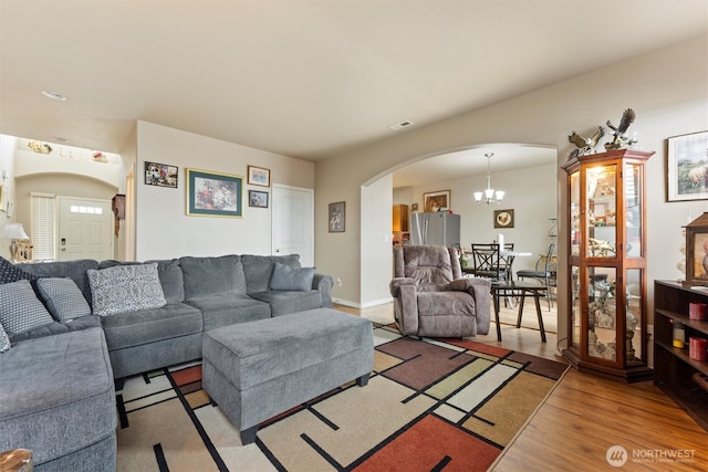 living area with arched walkways, wood finished floors, visible vents, and an inviting chandelier