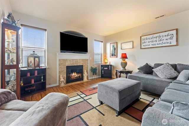 living room with wood finished floors, a tile fireplace, visible vents, and baseboards