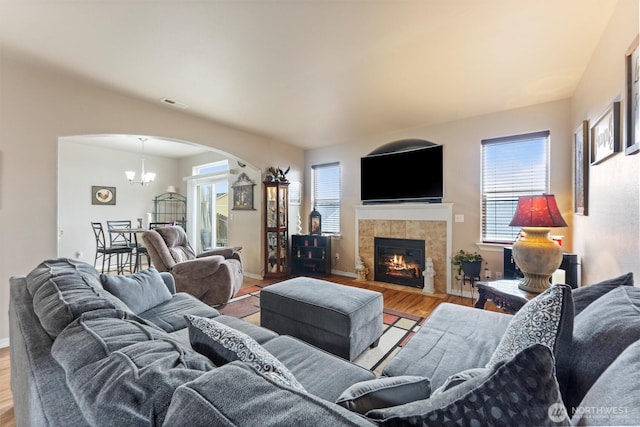 living room featuring a wealth of natural light, a notable chandelier, a tiled fireplace, and wood finished floors