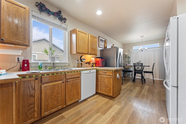 kitchen featuring brown cabinets, light wood finished floors, a sink, white appliances, and a peninsula