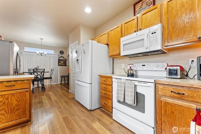 kitchen featuring white appliances, brown cabinetry, light countertops, light wood-style floors, and a chandelier