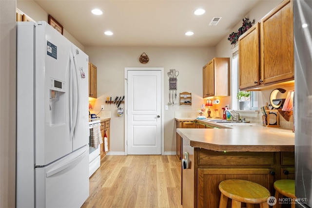 kitchen with white appliances, a peninsula, light countertops, light wood-style floors, and a sink