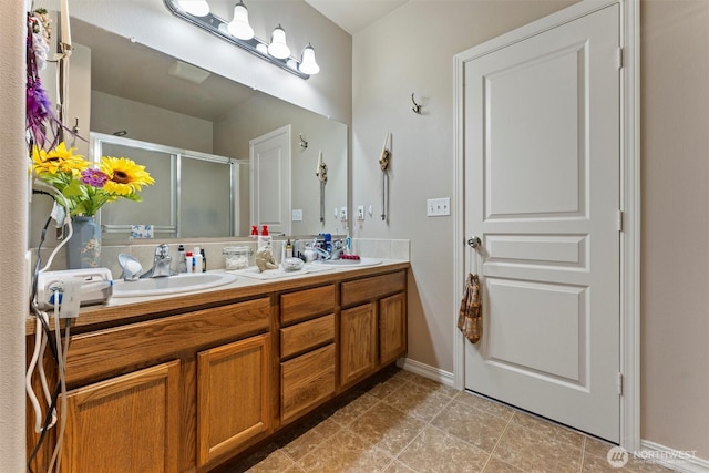 bathroom featuring a stall shower, a sink, baseboards, and double vanity