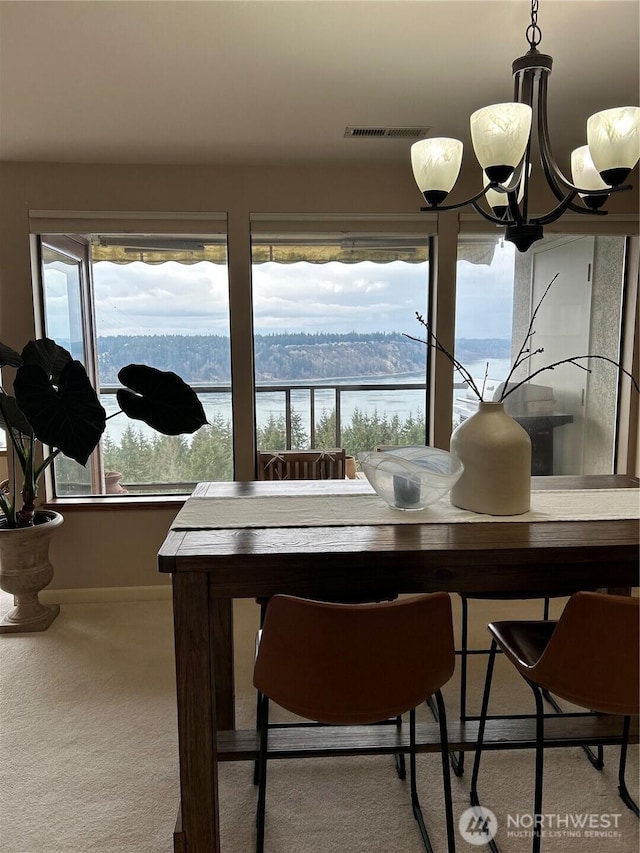 dining room with a water view, an inviting chandelier, visible vents, and carpet flooring