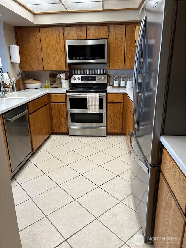 kitchen with light tile patterned floors, brown cabinetry, stainless steel appliances, light countertops, and a sink