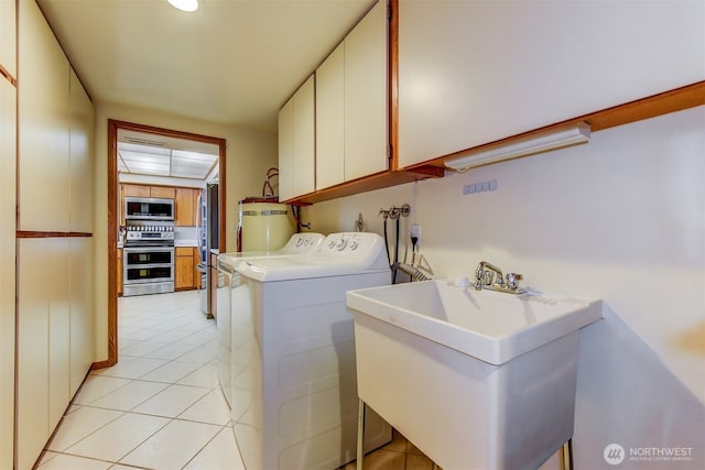 washroom with light tile patterned floors, a sink, water heater, washer and dryer, and cabinet space