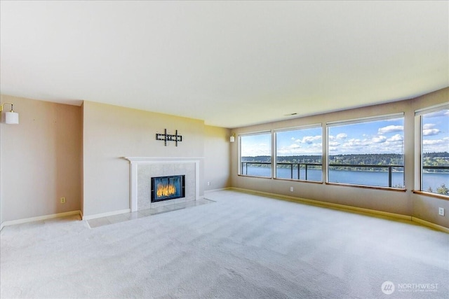 unfurnished living room featuring a water view, a tiled fireplace, carpet, and baseboards