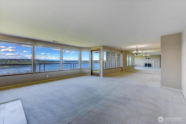 unfurnished living room featuring visible vents, a water view, baseboards, carpet floors, and a notable chandelier