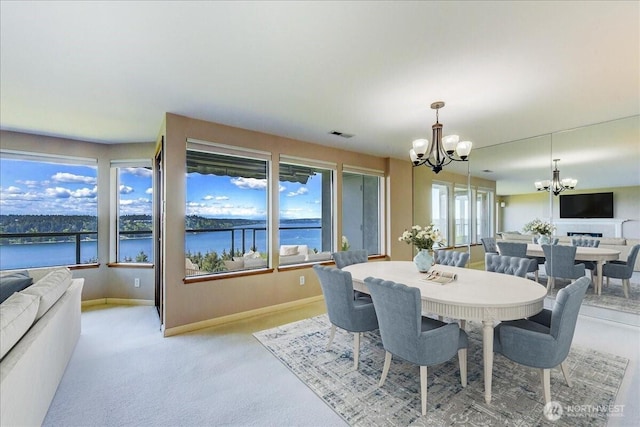 dining area with a water view, light carpet, baseboards, visible vents, and a notable chandelier