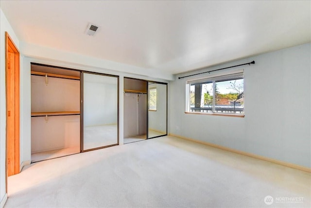unfurnished bedroom featuring two closets, baseboards, carpet floors, and visible vents