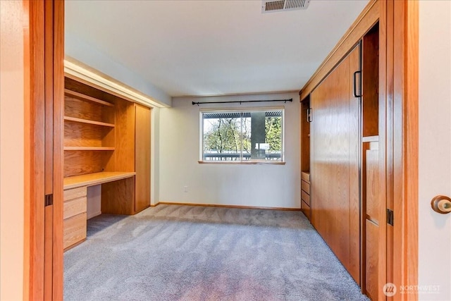 unfurnished bedroom featuring built in study area, baseboards, carpet floors, and visible vents