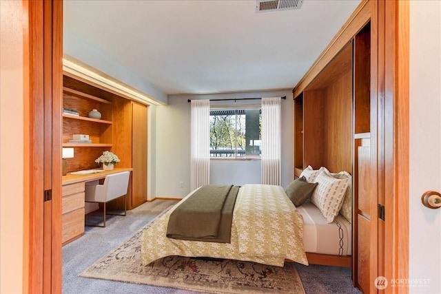 carpeted bedroom featuring built in desk, visible vents, and baseboards