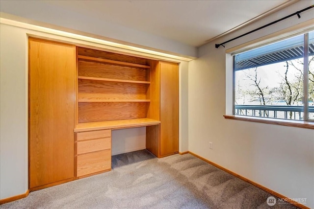 unfurnished bedroom featuring baseboards, light carpet, and built in desk