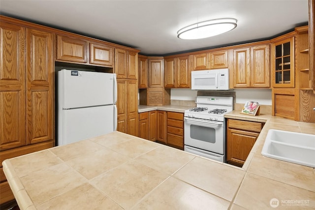 kitchen featuring white appliances, tile countertops, glass insert cabinets, tile patterned floors, and a sink