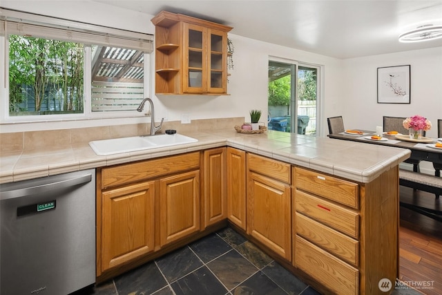 kitchen with tile countertops, a peninsula, a sink, dishwasher, and glass insert cabinets