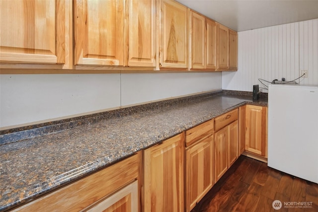 kitchen with dark wood-type flooring, refrigerator, and dark stone counters