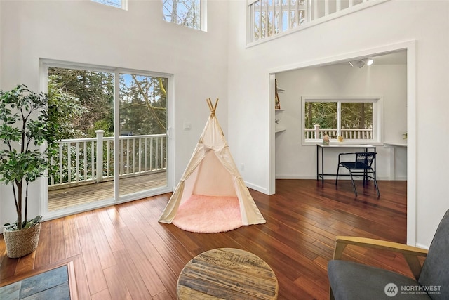 recreation room featuring baseboards, a high ceiling, and hardwood / wood-style flooring