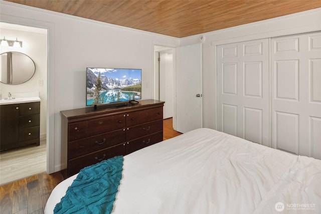 bedroom featuring a closet, wood ceiling, connected bathroom, a sink, and wood finished floors