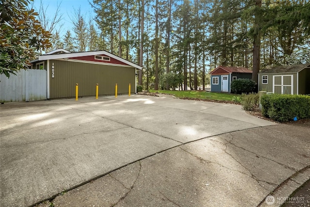 view of side of property featuring driveway, a storage shed, an outbuilding, fence, and a yard