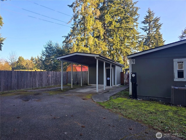 view of property exterior featuring aphalt driveway, central air condition unit, crawl space, fence, and a carport