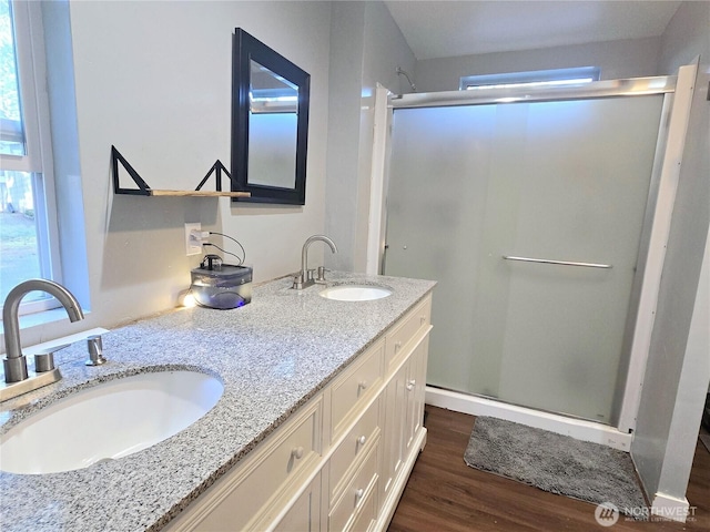 full bath featuring double vanity, a shower stall, a sink, and wood finished floors