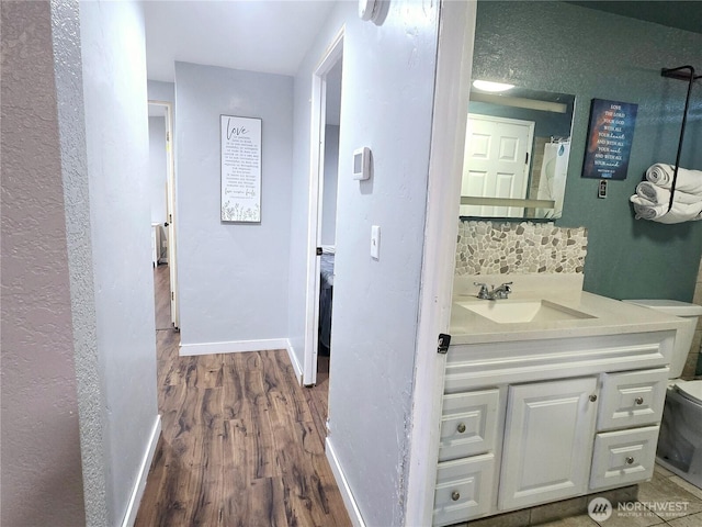 bathroom with toilet, wood finished floors, vanity, baseboards, and backsplash