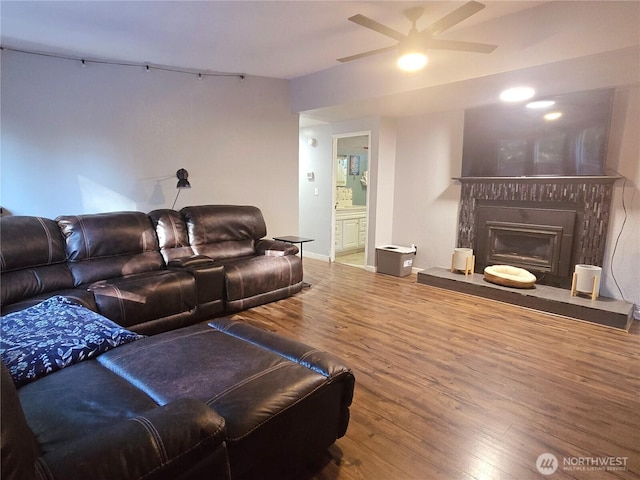 living room with ceiling fan, baseboards, a fireplace with raised hearth, and wood finished floors