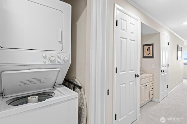 clothes washing area featuring crown molding, stacked washer and dryer, light carpet, laundry area, and baseboards