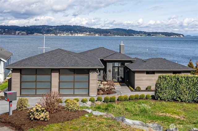 view of front of property with a water view, a garage, a chimney, and a shingled roof