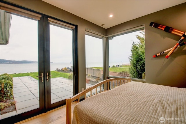 bedroom featuring access to exterior, french doors, light wood finished floors, a water view, and recessed lighting