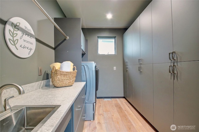 clothes washing area featuring light wood-style flooring, cabinet space, a sink, and washer / clothes dryer