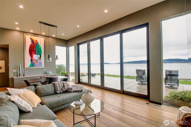 living area with light wood finished floors, visible vents, a water view, and recessed lighting