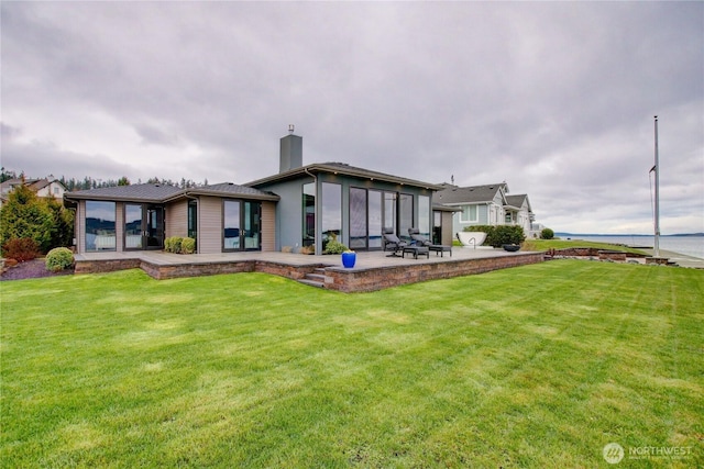 back of house featuring a lawn, a chimney, a sunroom, and a patio
