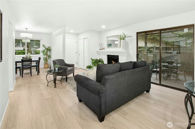 living room featuring recessed lighting, baseboards, a lit fireplace, and light wood finished floors