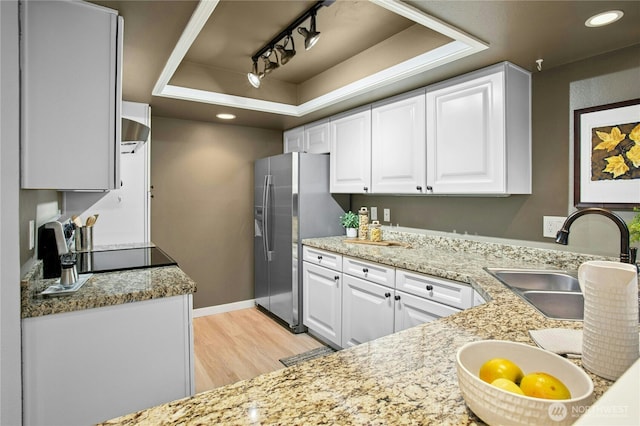 kitchen with light wood-type flooring, a sink, white cabinets, stainless steel fridge with ice dispenser, and a raised ceiling