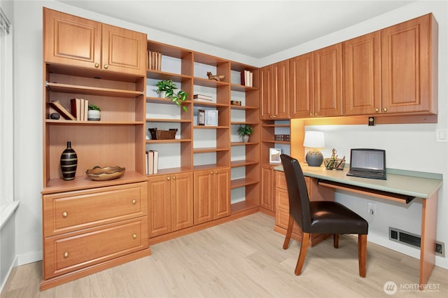 home office featuring visible vents, light wood finished floors, baseboards, and built in study area