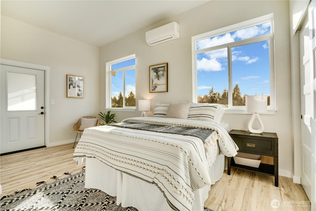 bedroom with baseboards, a wall unit AC, and light wood finished floors