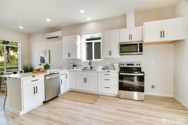 kitchen featuring white cabinets, appliances with stainless steel finishes, a wall mounted air conditioner, a peninsula, and a sink