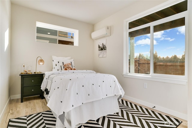 bedroom featuring light wood-type flooring, baseboards, and a wall mounted air conditioner