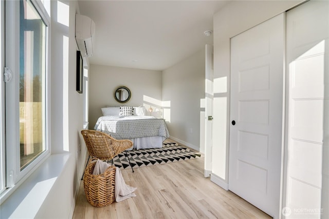 bedroom with light wood finished floors, baseboards, and an AC wall unit