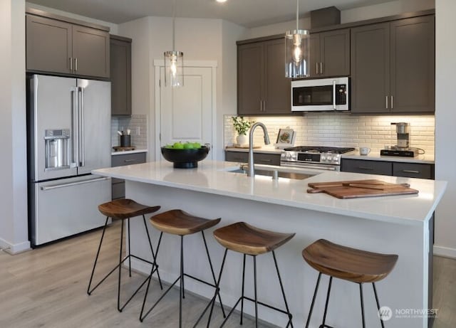 kitchen featuring tasteful backsplash, light countertops, light wood-style flooring, appliances with stainless steel finishes, and a sink