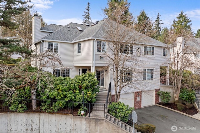 view of front of home featuring aphalt driveway, roof with shingles, a chimney, stairway, and a garage