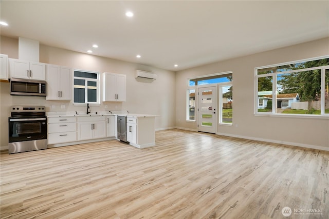 kitchen with light wood-type flooring, open floor plan, appliances with stainless steel finishes, white cabinets, and light countertops