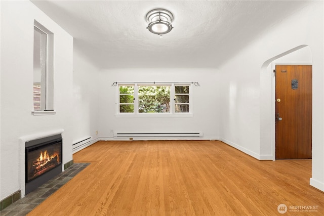 unfurnished living room featuring arched walkways, a baseboard radiator, a fireplace, wood finished floors, and baseboard heating