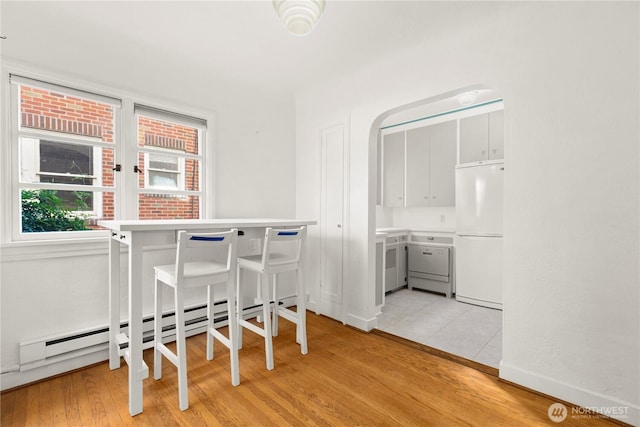 dining room featuring a baseboard radiator, light wood-style flooring, baseboards, and arched walkways