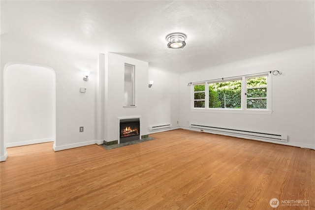 unfurnished living room with a baseboard radiator, light wood-style flooring, a baseboard heating unit, and a lit fireplace