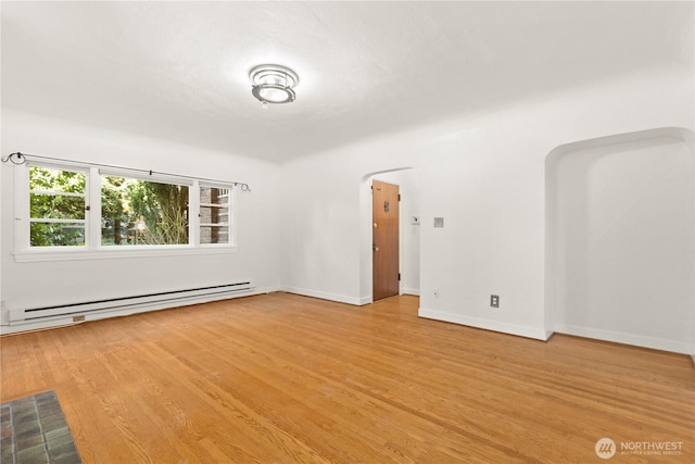 empty room featuring a baseboard radiator, arched walkways, baseboards, and wood finished floors