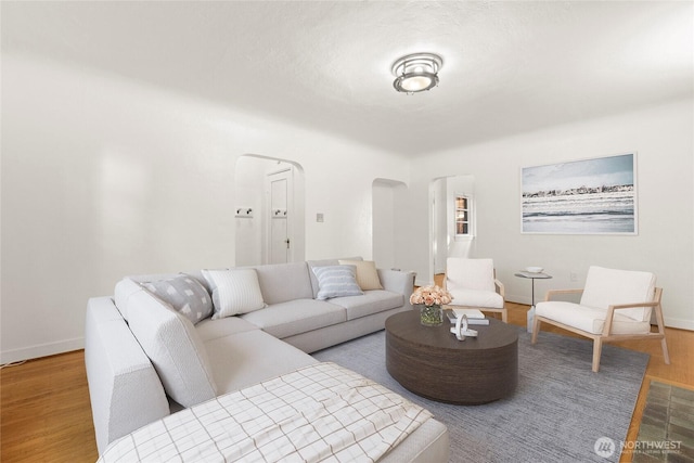 living room featuring baseboards, arched walkways, and wood finished floors