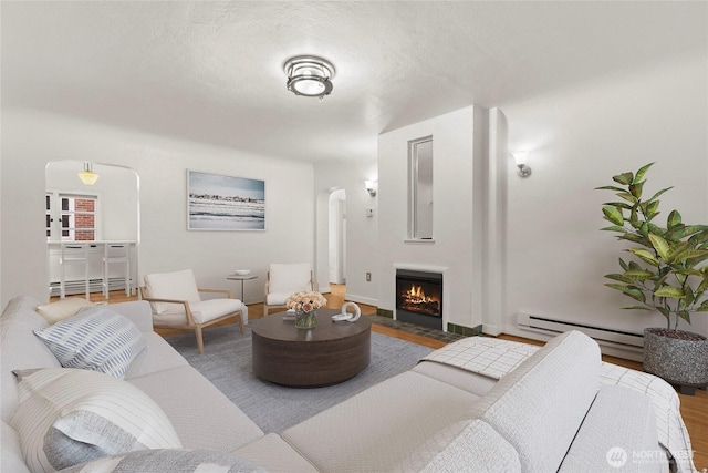 living area with arched walkways, a baseboard radiator, a fireplace with flush hearth, wood finished floors, and a textured ceiling