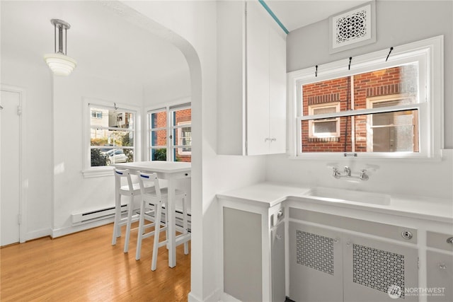 interior space featuring arched walkways, light wood finished floors, a sink, and visible vents